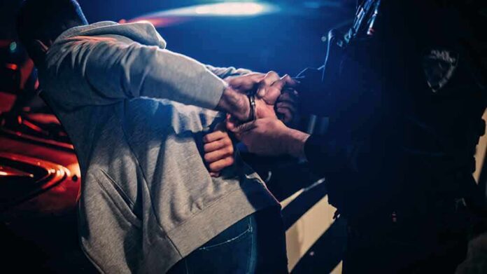 shutterstock_2232056691 Police officer handcuffing person at night by patrol car