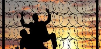 Silhouettes of people climbing a barbed wire fence at sunset
