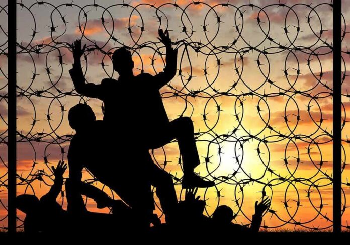 shutterstock_334479050 Silhouettes of people climbing a barbed wire fence at sunset