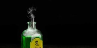 Glass bottle of green liquid labeled poison on wooden surface