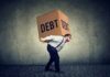 Trump Moves to Cancel $810 Million Man carrying a large box labeled debt on his back