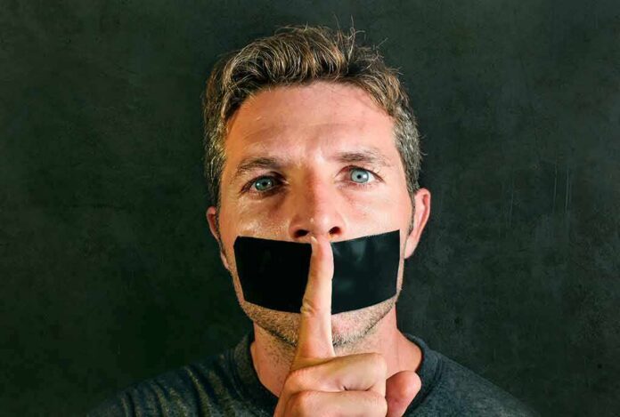 shutterstock_1092815663 man with tape over mouth holding a finger to lips