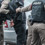 Police officers arresting a person beside a car