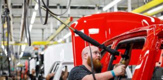 Factory worker assembling red vehicle body on production line