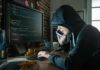 Person in hoodie using computer and phone at desk