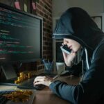 Trump Declares ‘Economic D-Day’ Against Iran Person in hoodie using computer and phone at desk