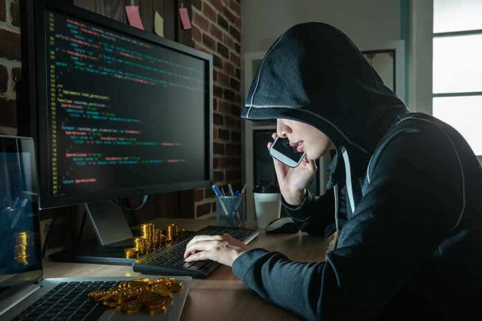 shutterstock_1166668681 Person in hoodie using computer and phone at desk