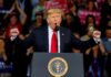 Donald Trump speaking at a rally podium with arms raised
