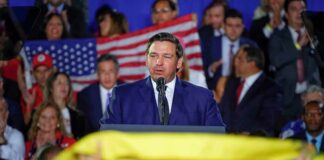 man in suit speaking at a podium during a rally