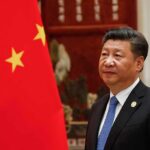 Xi Jinping standing beside a Chinese flag