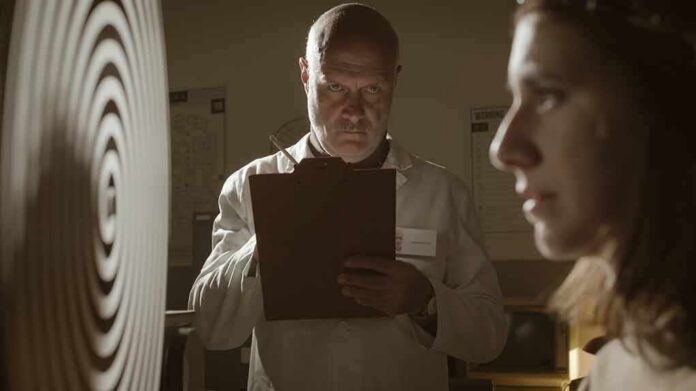 shutterstock_1527380264 Scientist with clipboard observes woman beside spiral target