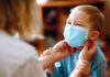 child wearing a surgical mask being adjusted by an adult