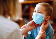 child wearing a surgical mask being adjusted by an adult