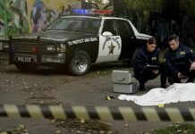 FBI agents examine a covered body at a taped-off crime scene
