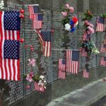 Ground Zero Showdown Erupts Memorial wall adorned with American flags and flowers
