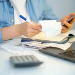 Person reviewing receipts with phone, notebook, and laptop