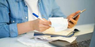 Person reviewing receipts with phone, notebook, and laptop