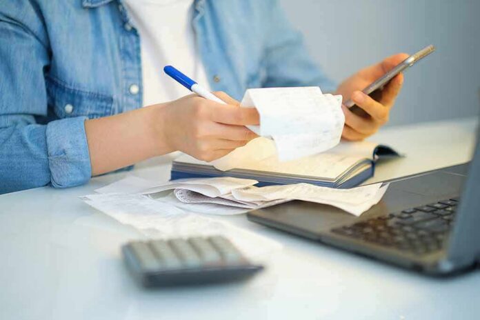 shutterstock_1918768208 Person reviewing receipts with phone, notebook, and laptop