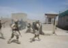 Iran-Backed Drone Kills U.S. Troops Soldiers in desert uniforms run past a checkpoint amid dust