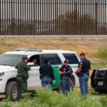 law enforcement officers confer beside patrol vehicles near a border fence