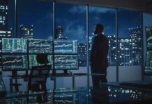 He Compared AI to Nukes Then Said Keep Going Trader in a dark office with multiple stock monitors and city skyline at night