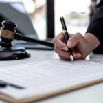 80 People Charged in $245M PPP Heist Hand signing legal document beside gavel and laptop