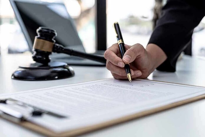 shutterstock_2103308165-2 Hand signing legal document beside gavel and laptop