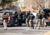 Police and sheriff officers gather around vehicles on a suburban street