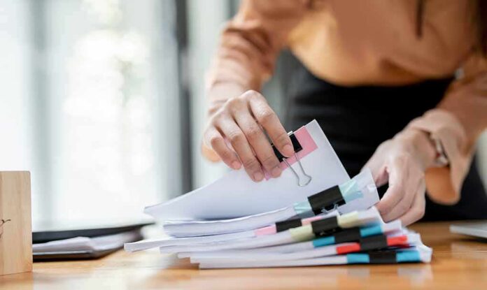 shutterstock_2197526607 Hands organizing stacked documents with binder clips