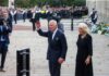 Charles, Prince of Wales waves while walking outdoors with a woman