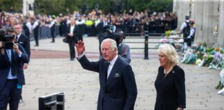 Charles, Prince of Wales waves while walking outdoors with a woman