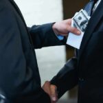 The Election System Was Built to Make This Perfectly Legal Businessmen handshake as cash is slipped into a suit pocket