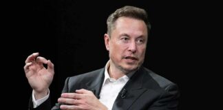 Elon Musk speaking in a black suit against a dark background