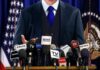 A speaker at a press conference with multiple microphones in front of them