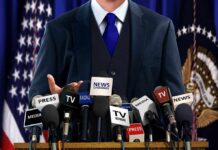 A speaker at a press conference with multiple microphones in front of them
