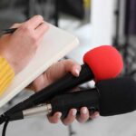 Warship Stage, Vance Drops Culture Hammer Journalist holding two microphones while writing in a notebook