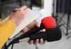 Detroit Schools Now Bribe Students to Attend Class Journalist holding two microphones while writing in a notebook