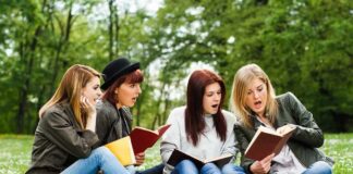 Group of young women reading books on grass in a park