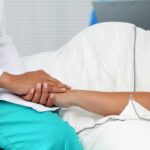 Healthcare worker holding a patient's hand in a hospital bed