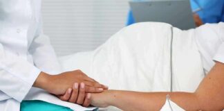 Healthcare worker holding a patient's hand in a hospital bed