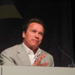 Arnold Schwarzenegger speaking at a podium with a microphone