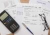 War Tax at the Pump? Utility bills with calculator, pen, and eyeglasses on a desk