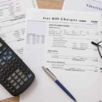 Utility bills with calculator, pen, and eyeglasses on a desk