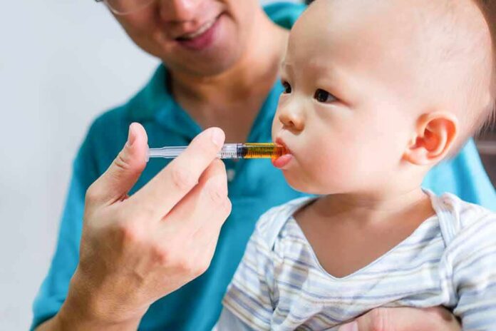 shutterstock_602417219 Baby taking liquid medicine from an oral syringe held by an adult