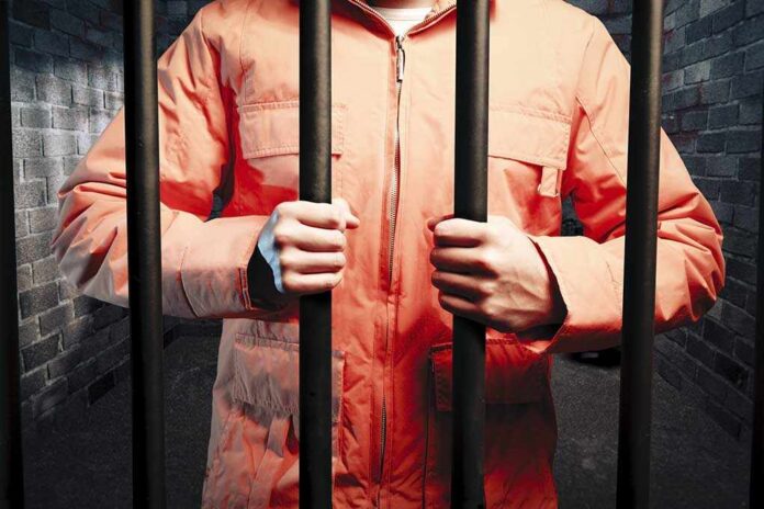 Dark,Prison,Cell,At,Night Person in an orange jumpsuit gripping prison bars in a dark cell