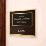 Senator Dies Suddenly — Cause Still Missing office wall plaque with black and gold nameplate and room number