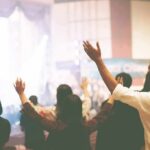 Pastor Gets Life for Raping Child as Wife Helped Enable Abuse Audience raising hands at indoor event