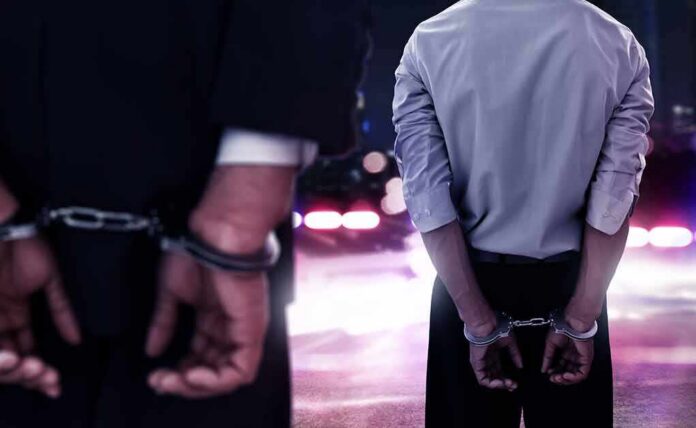 shutterstock_1038568315 Two men in handcuffs with police lights in the background