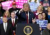 Donald Trump speaking at a rally podium, pointing toward the audience