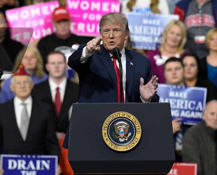 Donald Trump speaking at a rally podium, pointing toward the audience